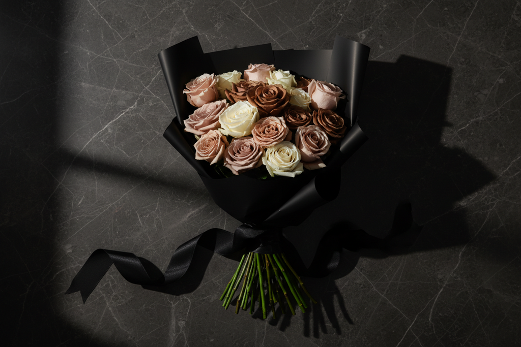 Top down flat lay of nude roses in matte black wrap with black satin ribbon